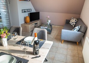 A modern living room with a dining area, a sofa, a TV, and a small table with a bottle and glasses.