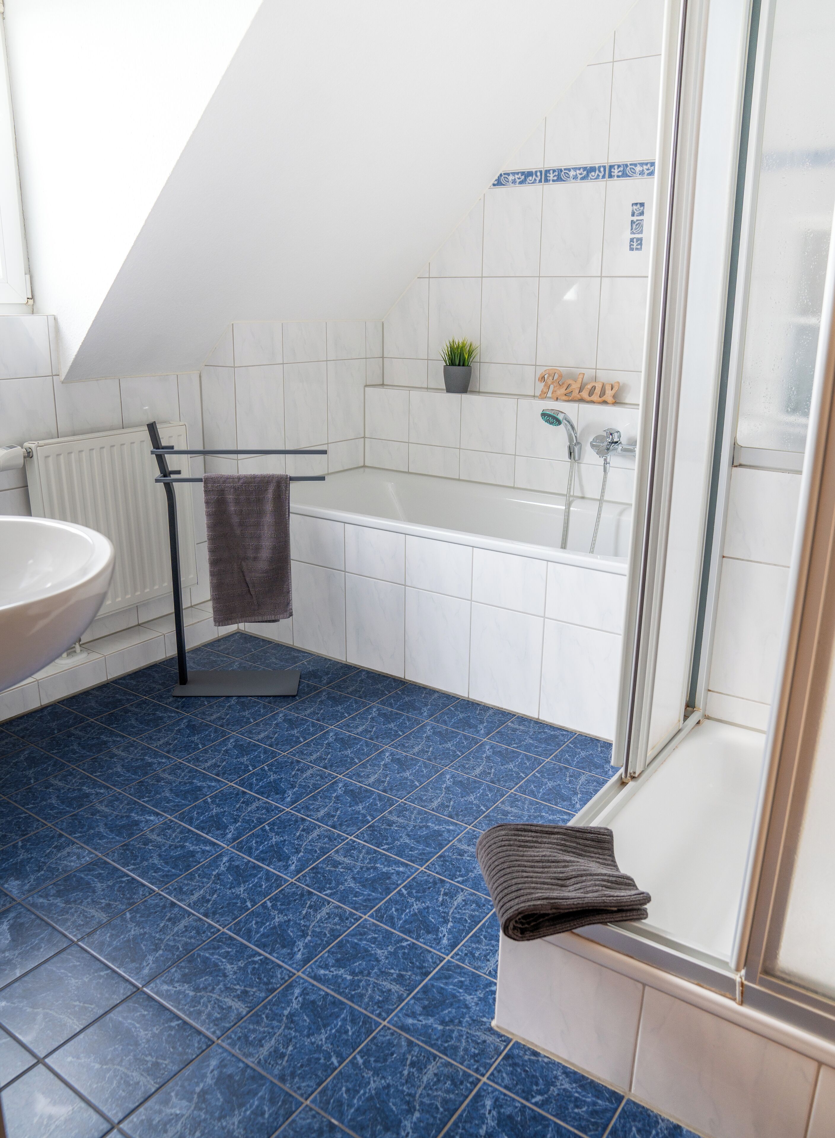 Ein modernes Badezimmer mit einer Badewanne, einer Glastrennwand-Dusche, einem weißen Waschbecken und einem blau gefliesten Boden.