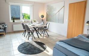 A modern room with a dining table set for four, a sofa, a large window with a view, and a door.