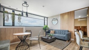 A modern living room with a grey sofa, a round table, and two chairs. There is a large window with plants and a view of the outdoors. - Go Living 601 · Amazing Luxury 2BR Apt Poblado - 2AC and coworking (Medellín)