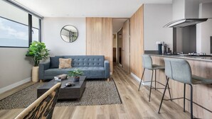 A modern living room with a grey sofa, a coffee table, and a small plant. There is a kitchen area with a bar counter and stools. - Go Living 601 · Amazing Luxury 2BR Apt Poblado - 2AC and coworking (Medellín)