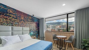 Een moderne hotelkamer met een groot bed, stadszicht, een kleintje tafeltje en een balkon.