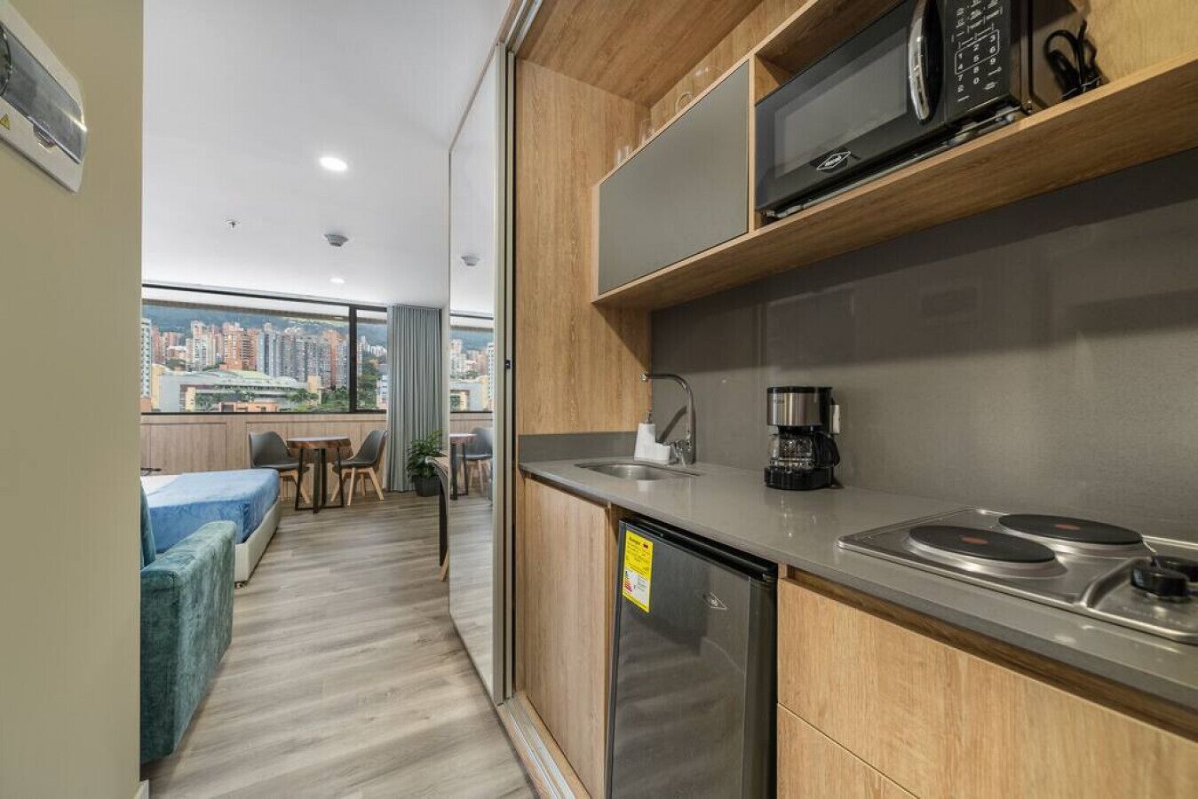 Una cocina compacta equipada con microondas, cafetera y lavavajillas. Se aprecia un comedor con mesa y sillas al fondo.