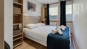 Een slaapkamer met een bed, houten planken, een raam met gordijnen en een schilderij aan de muur.