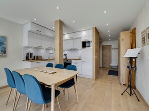 A modern kitchen with white cabinets, a wooden dining table with blue chairs, and a music stand with sheet music.