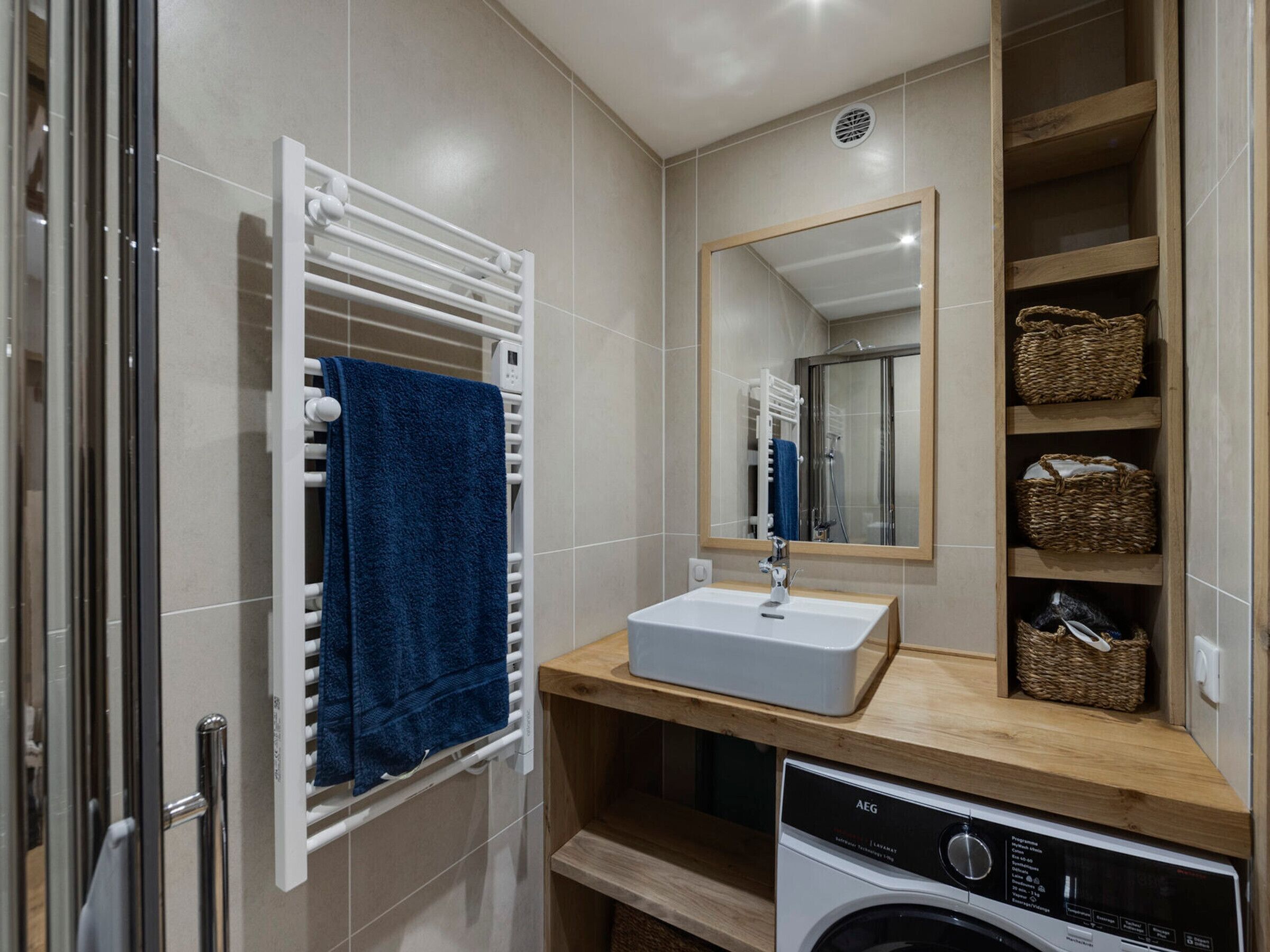 Un bagno moderno con lavatrice integrata, un lavandino bianco e un portasci con un asciugamano blu.