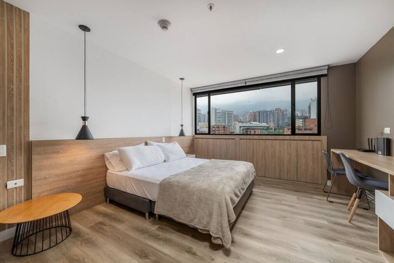 A modern bedroom with a bed, a desk, and a view of the city.