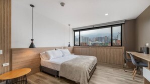 A modern bedroom with a bed, a desk, and a view of the city.