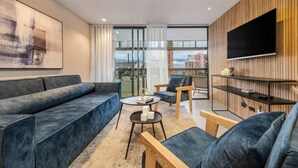 Een moderne woonkamer met een bank, fauteuils, een salontafel en een televisie bevestigd aan een houten wand.