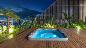 Een hottub op een houten terras met uitzicht op de stad 's nachts.