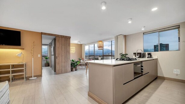Una cocina moderna con una isla central, electrodomésticos integrados y grandes ventanales que ofrecen vistas a la ciudad.