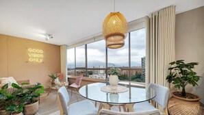 Una sala de estar moderna con una mesa de vidrio, sillas de mimbre y vista de la ciudad a través de amplias ventanas.