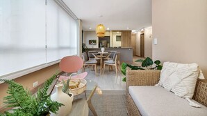 Una sala de estar moderna con un sofá, una mesa de comedor y sillas. Se observa un área de cocina al fondo con una lámpara colgante.