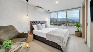 Un dormitorio moderno con una cama grande, vistas de la ciudad y un balcón con plantas.