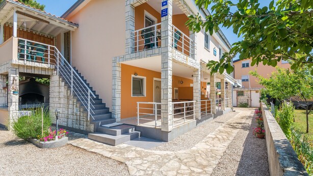 A two-story building with a stone staircase, a covered outdoor seating area, and a small garden with potted plants. - Apartments Horvatic (Vir)
