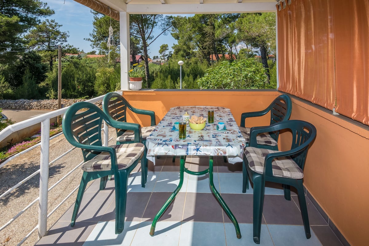 An outdoor patio with a table and chairs, surrounded by a railing and a view of trees and houses.