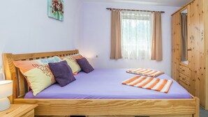 A wooden bed with a purple mattress, multiple pillows, and a bedside table with a lamp. - Apartments Horvatic (Vir)