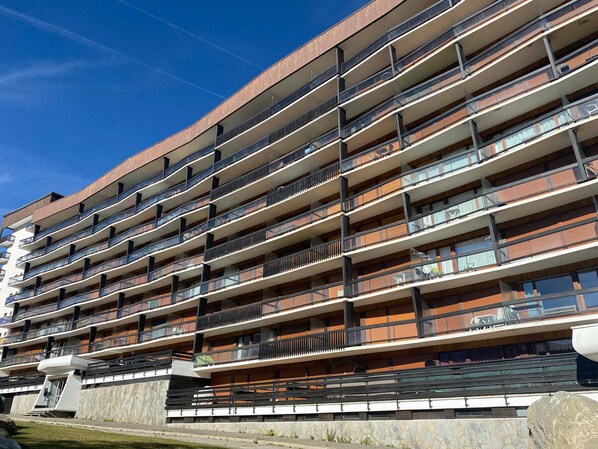 A multi-story building with balconies, a stone base, and a clear sky. - Spacious renovated apartment with terrace and parking in Tignes (Tignes)