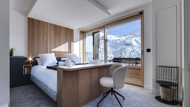 Una moderna camera d'albergo con un letto, una scrivania e vista su una montagna innevata.