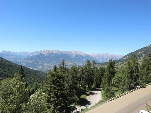 A road winding through a mountainous area with dense forests and distant mountains under a clear sky.