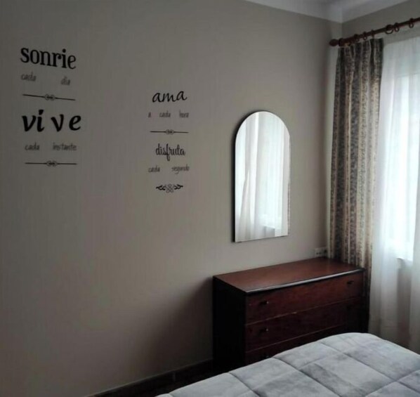 Un dormitorio con cama, cómoda y espejo. Hay decoraciones en la pared con texto en un idioma extranjero.