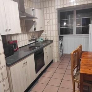 Una cocina compacta con armarios blancos, una encimera negra, una estufa y una lavadora.