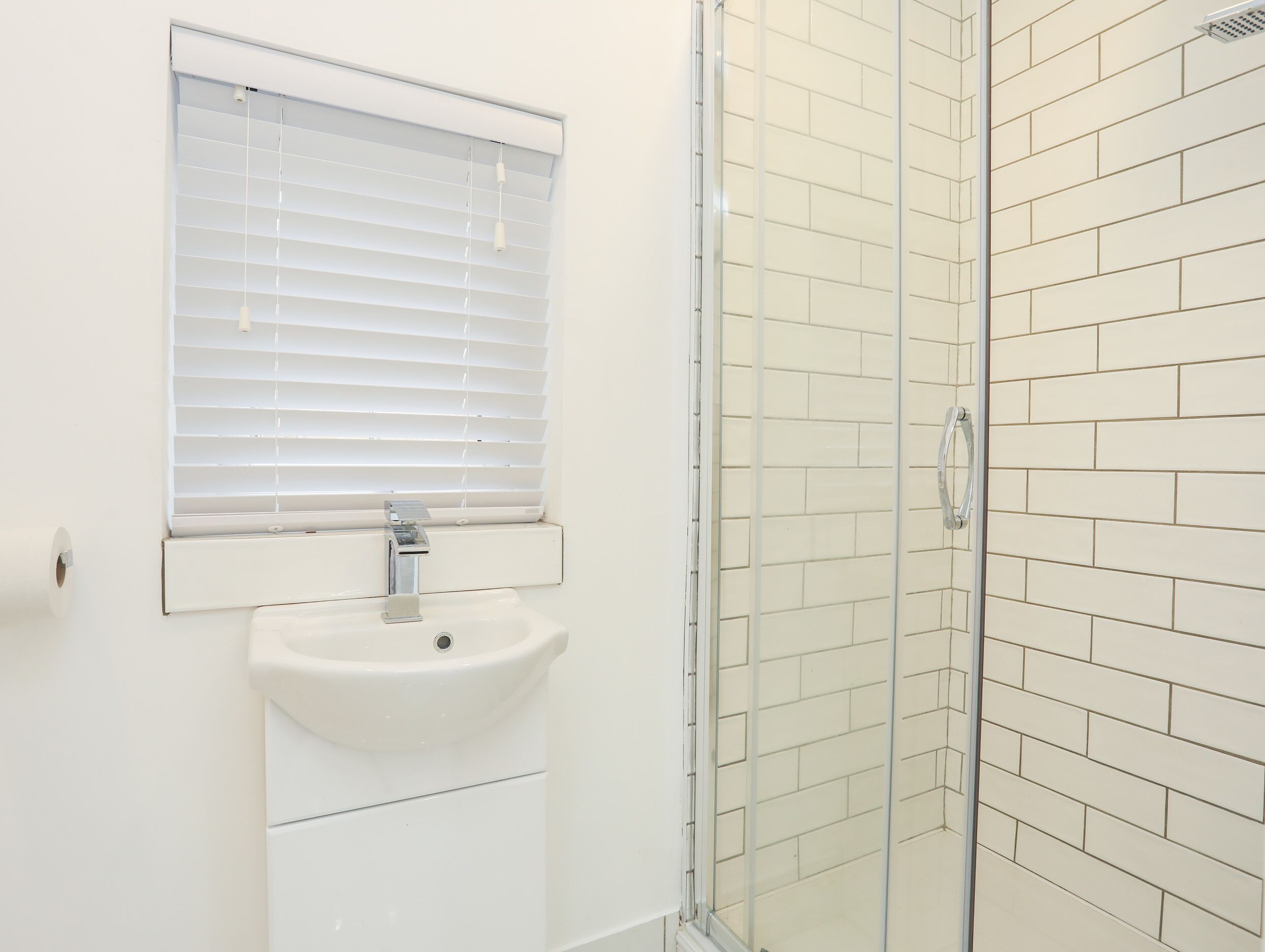 Un bagno con un lavandino bianco, una finestra con persiane e un box doccia in vetro.