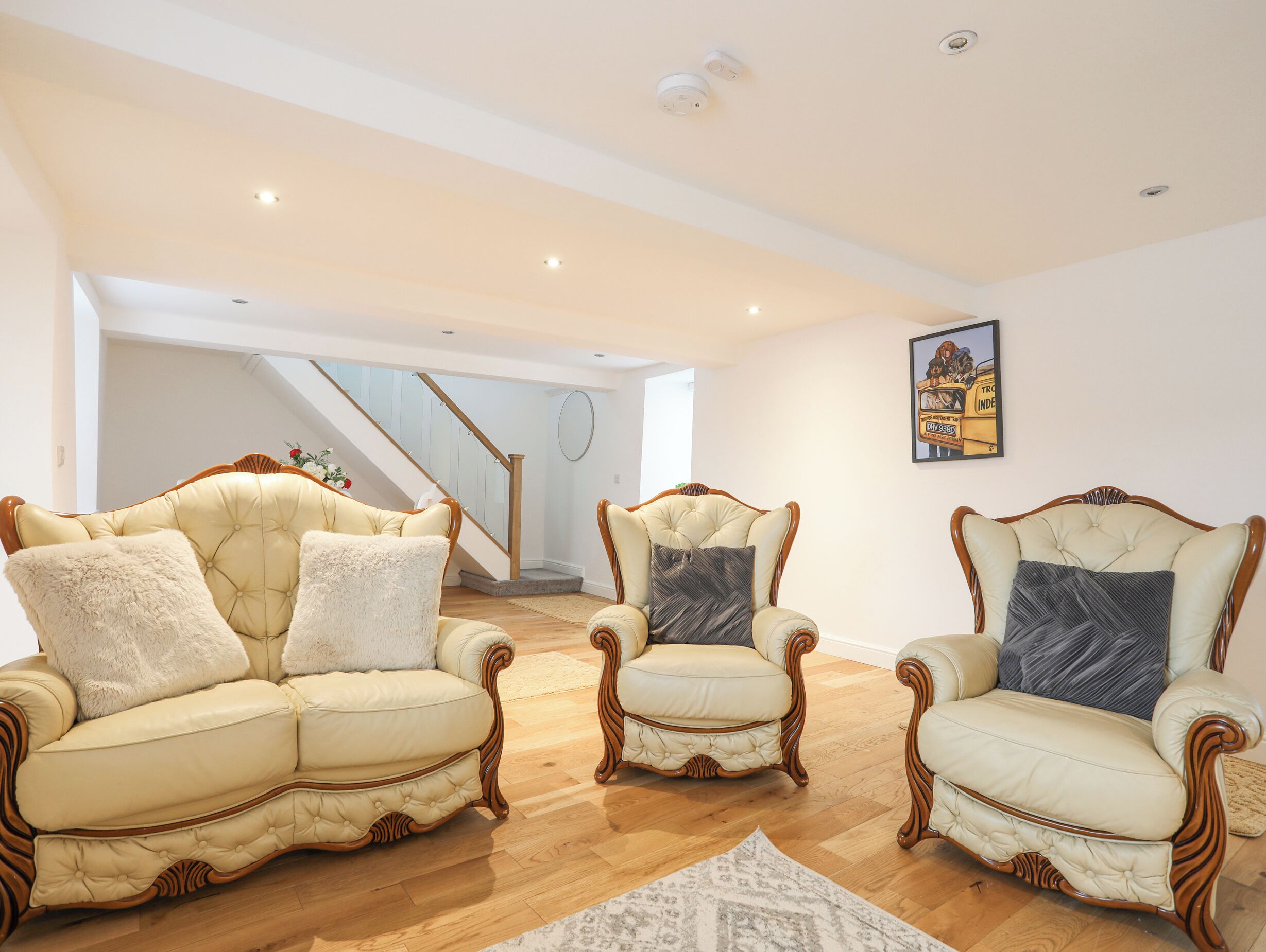 A spacious living room with a wooden staircase, leather armchairs, and a framed picture on the wall.