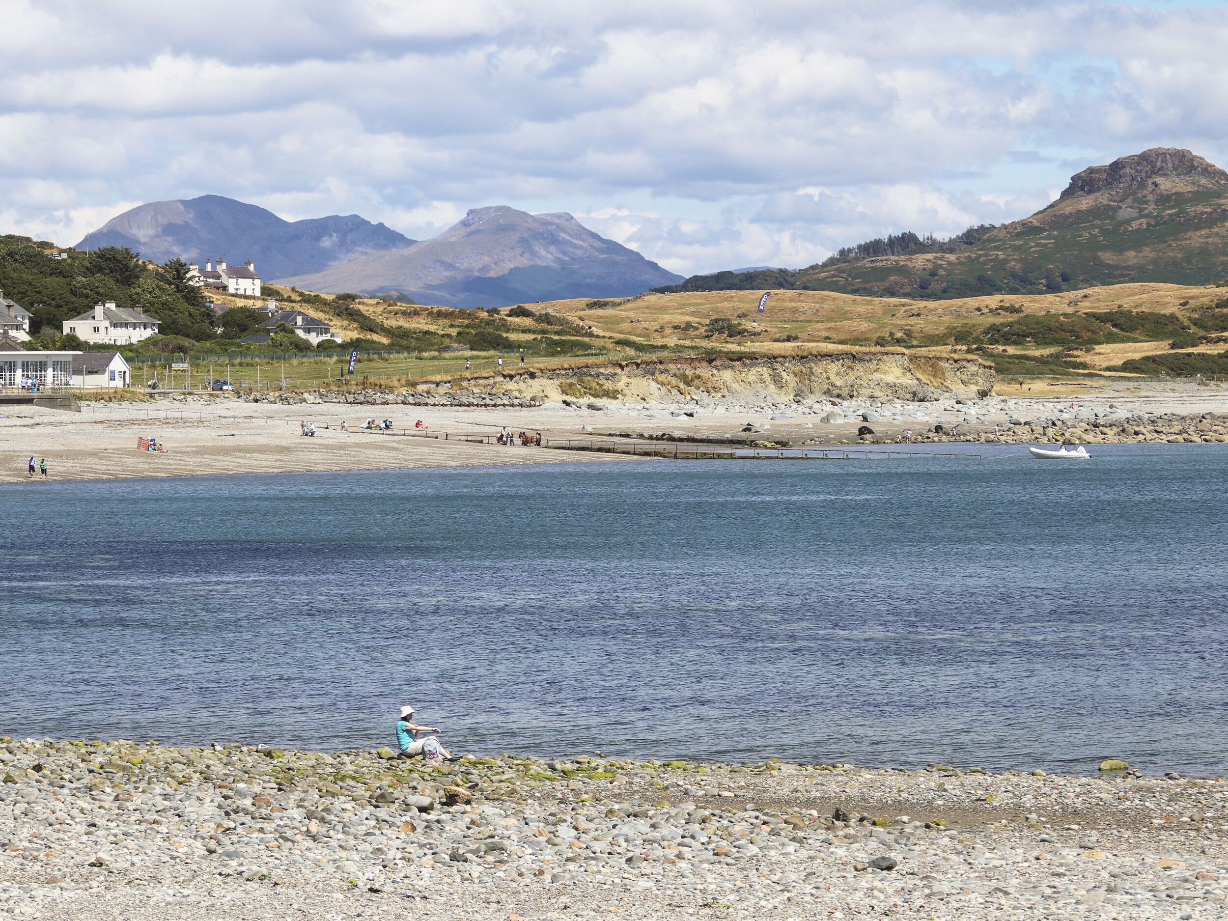 A coastal area with a rocky beach, a small boat, and a person fishing.