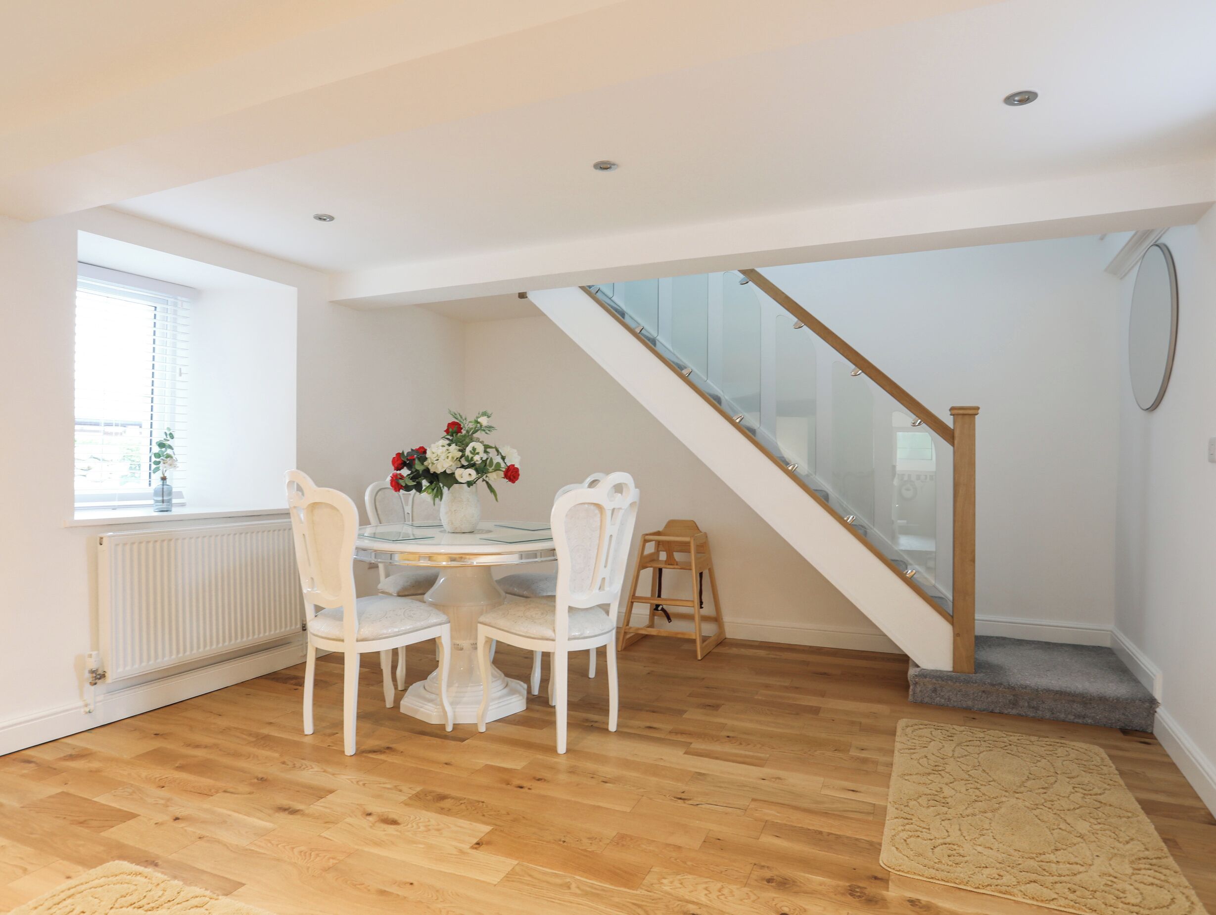 A dining area with a round table, white chairs, and a vase of flowers. A wooden ladder is next to the staircase.