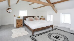 Ein Schlafzimmer mit Holzbalkendecke, einem Bett mit weißer Bettwäsche, zwei Nachttischen mit Lampen und einem dekorativen Teppich.