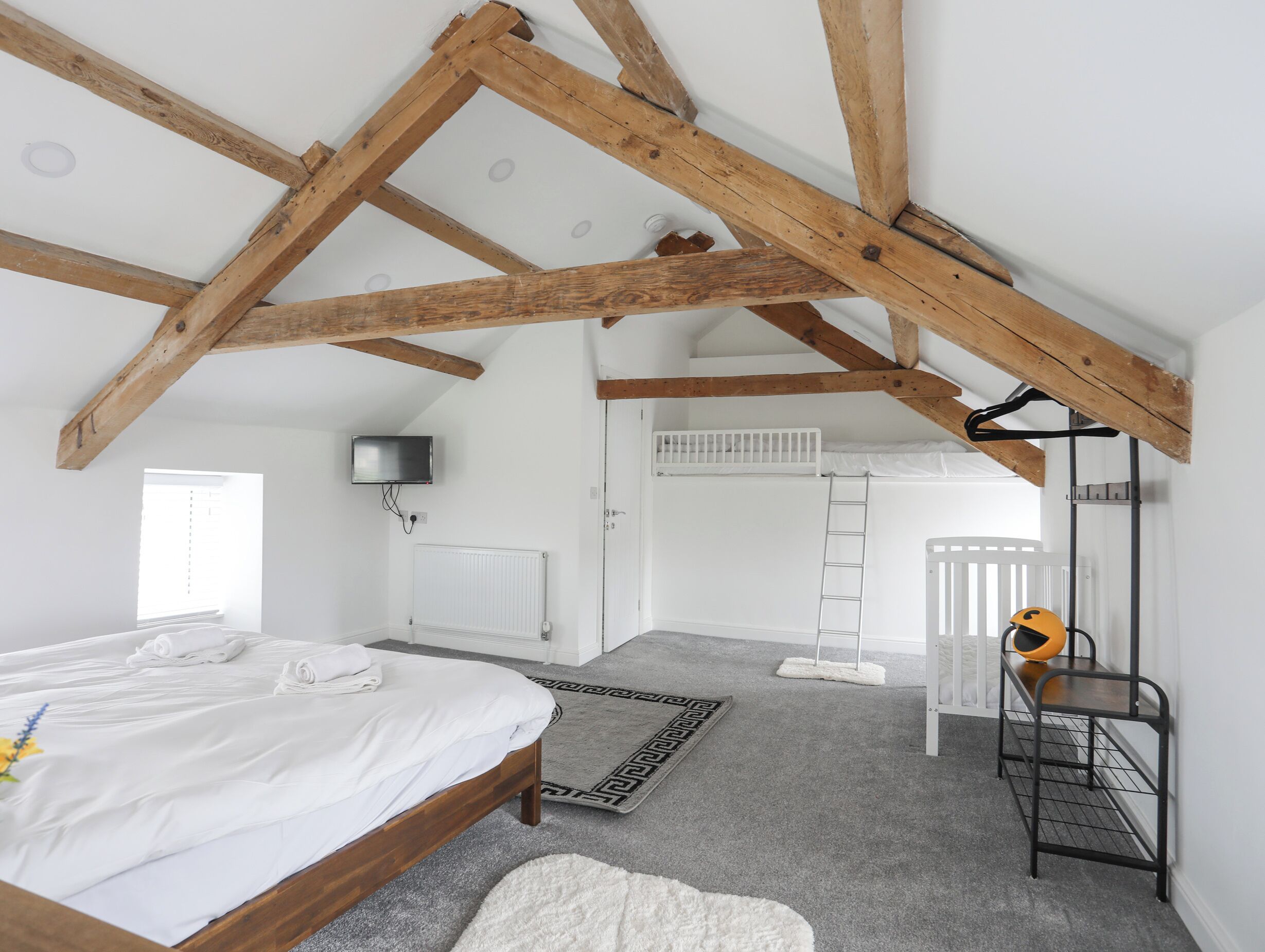 A bedroom with a wooden ceiling, a bed, a TV, a radiator, a white door, and a ladder.