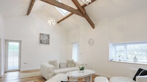 Ein geräumiges Wohnzimmer mit hohen Decken, Holzbalken, einer weißen Sofagarnitur, einem runden Couchtisch und einem Fenster mit Blick.