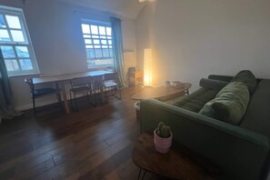 Ein Wohnzimmer mit einem grünen Sofa, einem Couchtisch aus Holz mit einem Kaktus, einem Essbereich mit Tisch und Stühlen und einer Lampe.