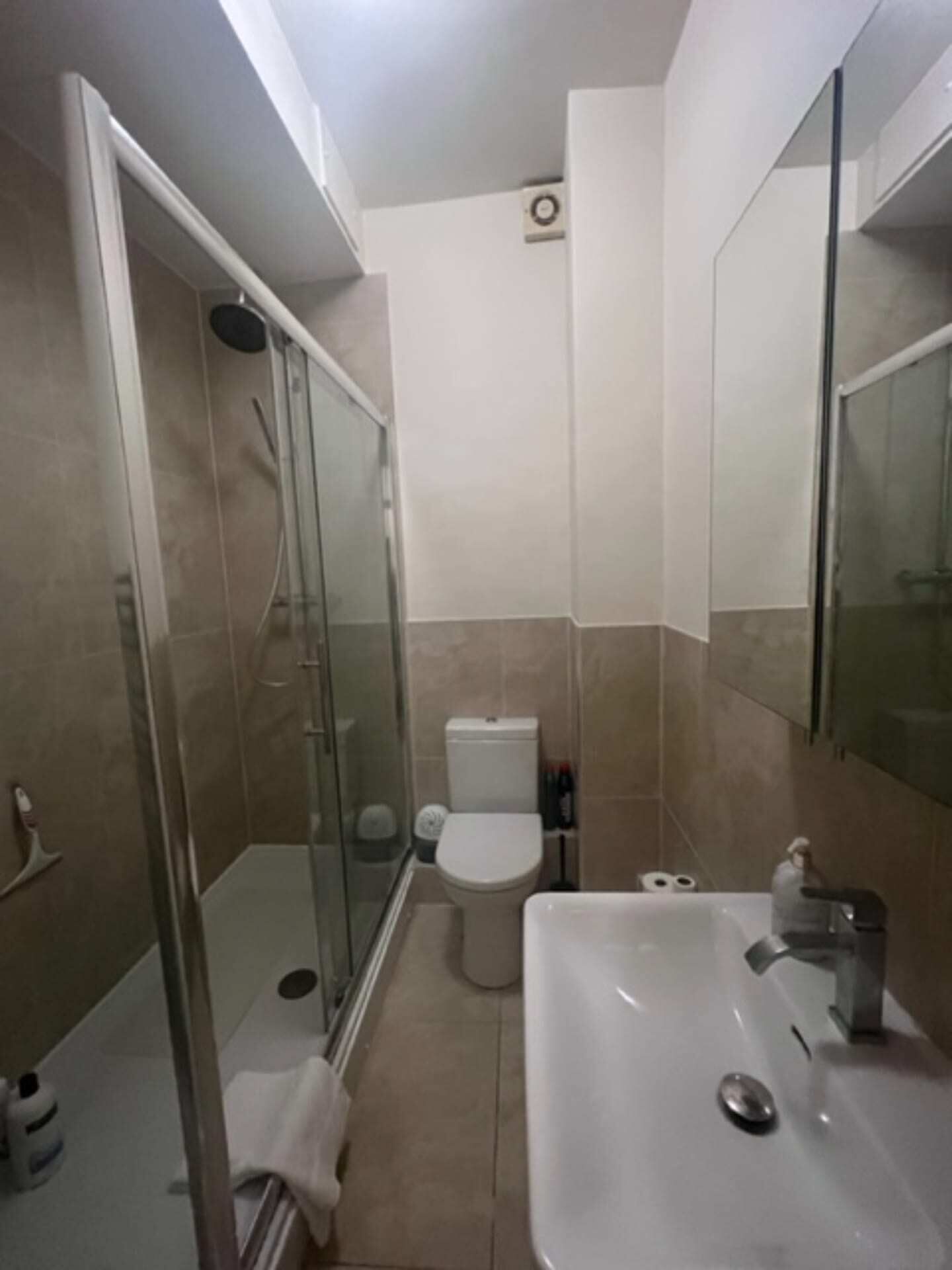 A modern bathroom with a glass-enclosed shower, a white toilet, and a sink with a mirror above it.