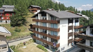 A multi-story building with balconies, labeled 'Atlantic,' surrounded by forested hills. - Classy Studio in Saas-fee, Alps, Switzerland (Saas-Fee)