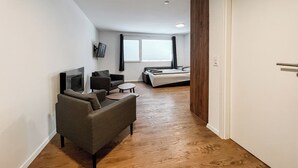A compact living space with a sofa, a small table, a bed, and a TV mounted on the wall. - Classy Studio in Saas-fee, Alps, Switzerland (Saas-Fee)