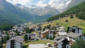 A mountainous village with residential buildings, a winding road, and a valley with a glacier in the background. - Classy Studio in Saas-fee, Alps, Switzerland (Saas-Fee)