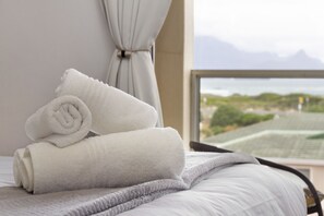 Un lit bien fait, avec des serviettes blanches pliées en rouleaux, et une vue sur un paysage montagneux par la fenêtre.