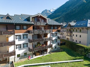 Un edificio de varios pisos con balcones, un patio y montañas al fondo.
