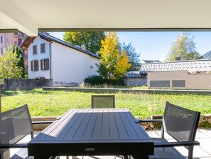An outdoor patio with a table and chairs, a view of a house, and a tree with yellow leaves.