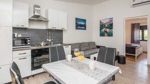 Una cocina moderna con armarios blancos, horno empotrado y comedor con mesa de mármol y sillas negras.