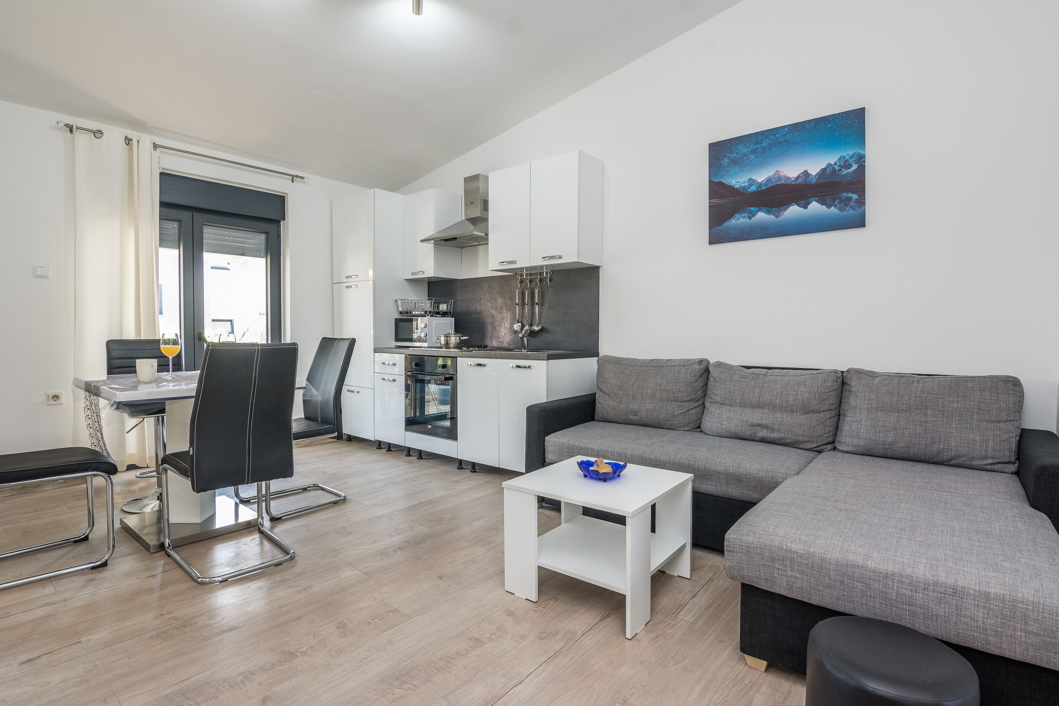 Ein modernes Wohnzimmer mit einem grauen Sofa, einem kleinen weißen Tisch und einem Essbereich mit einem schwarzen Stuhl und einem weißen Tisch.