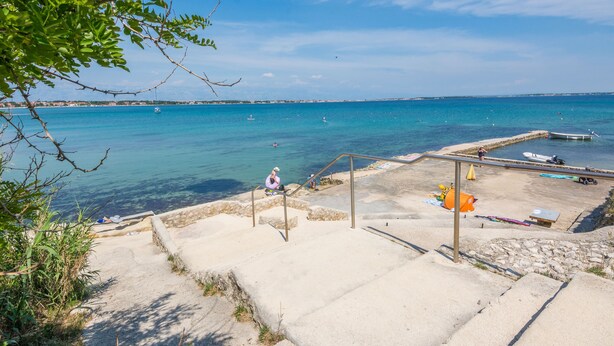Una zona costera con vista despejada al mar, una playa arenosa y una escalera que baja hacia el agua.