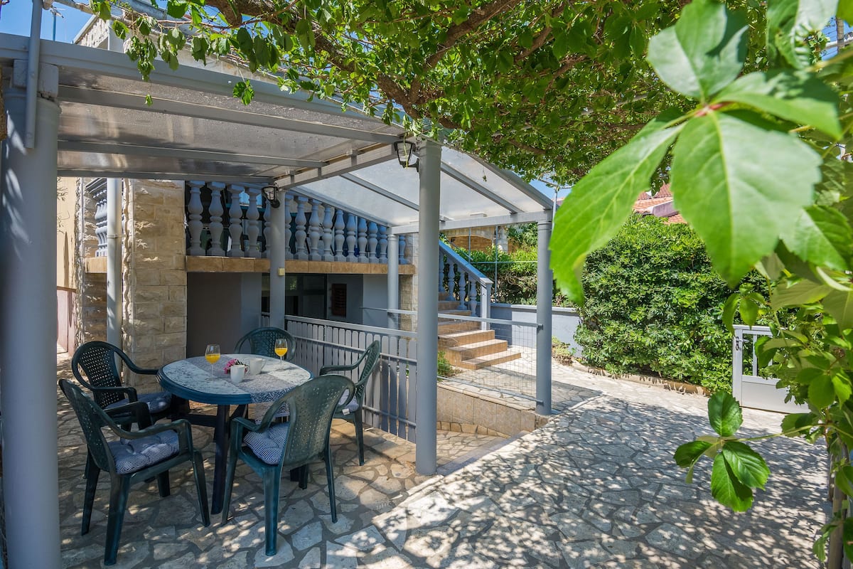 An outdoor patio with a covered seating area, stone flooring, and a view of a building with a staircase.