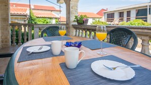 Una mesa redonda de madera con superficie de vidrio, preparada para el desayuno, con dos tazas blancas, un vaso de zumo de naranja y un plato con cubiertos.