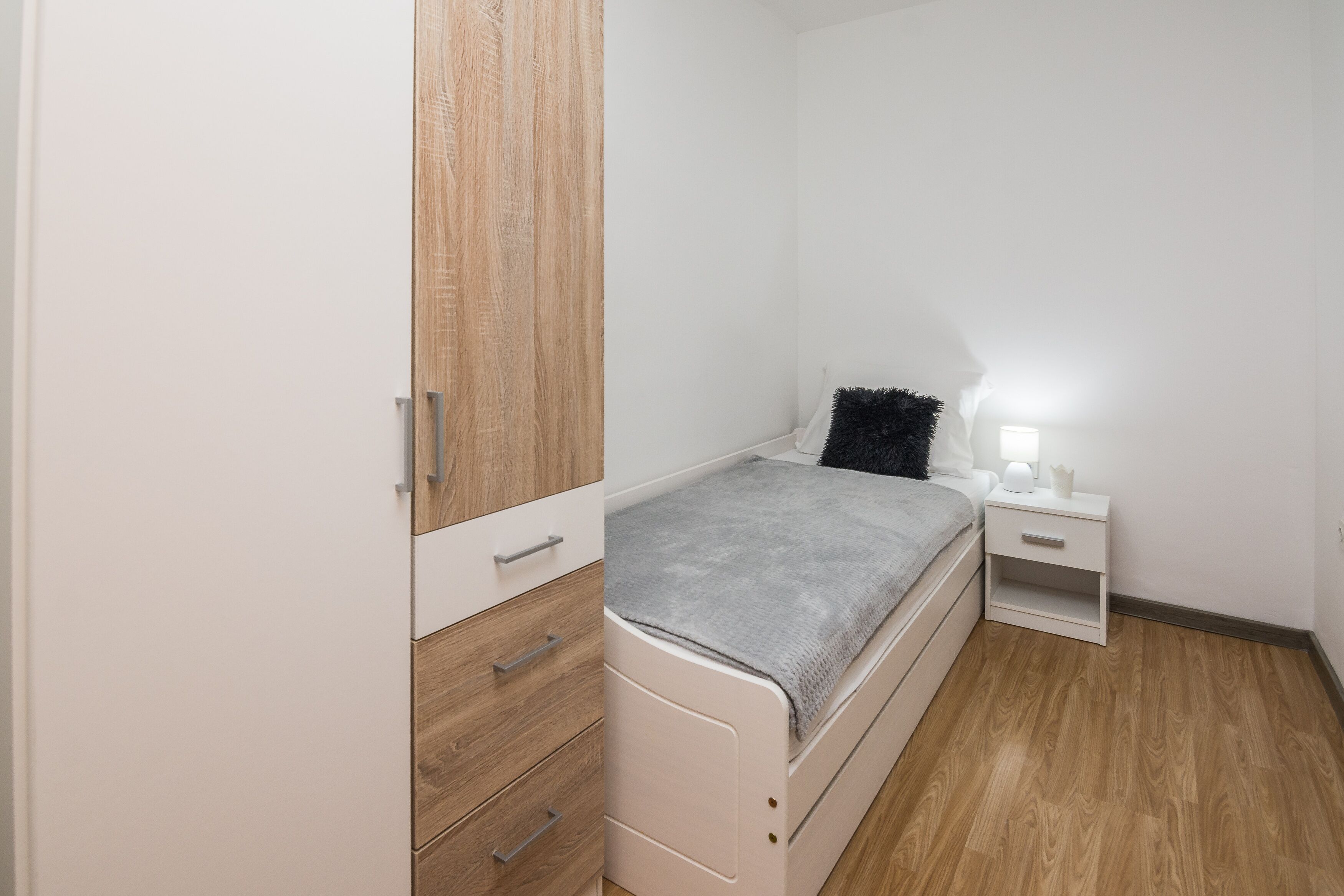 A bedroom with a bed, a nightstand, a wardrobe, and a bedside table.