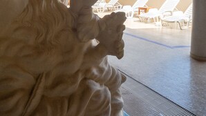 A stone sculpture of a woman with long hair in a covered outdoor area with lounge chairs.