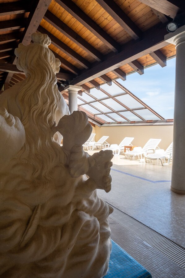 Escultura de piedra de una mujer con cabello largo en un espacio exterior cubierto con sillones de descanso.