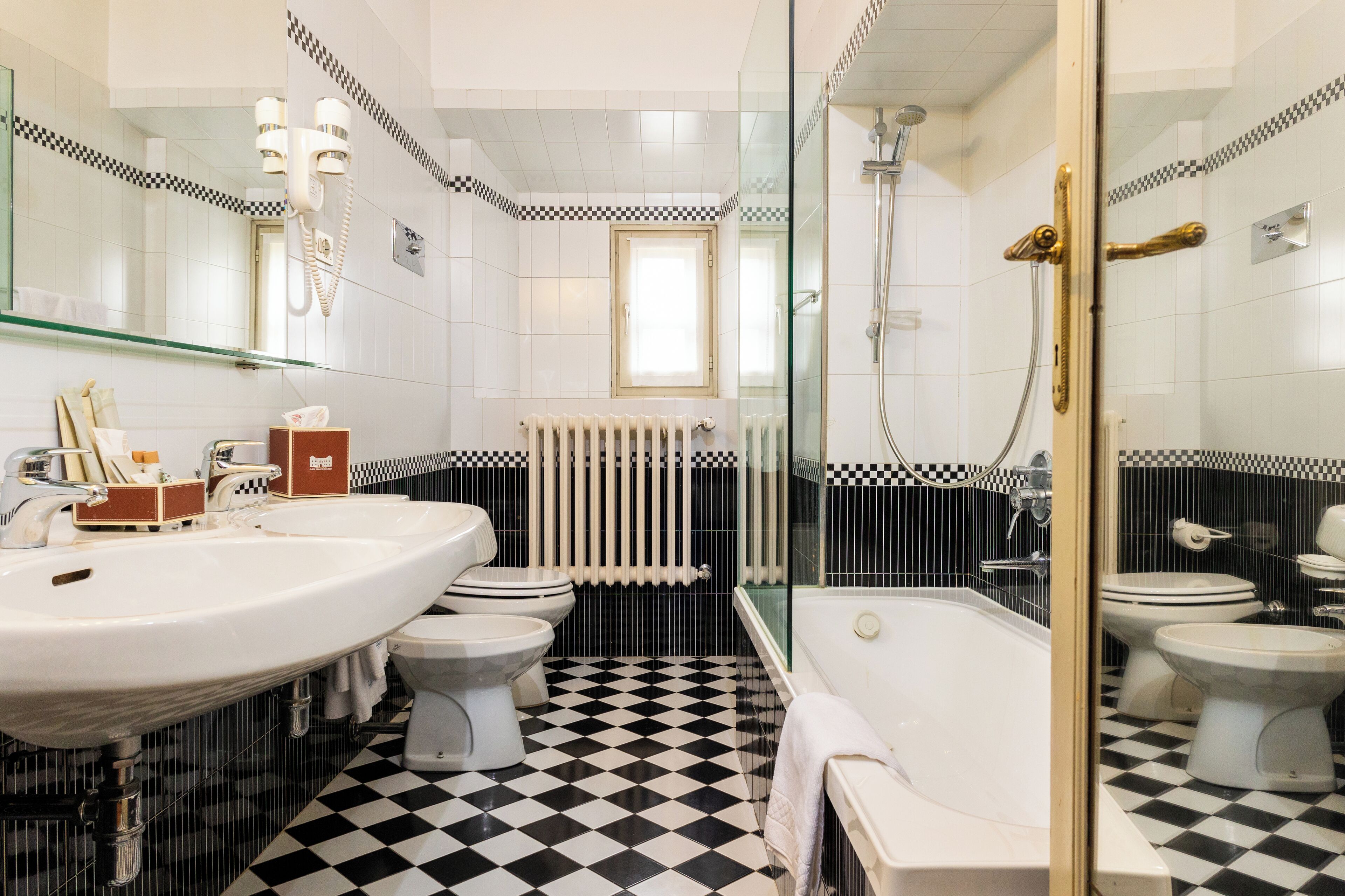 Un baño con un lavamanos grande de color blanco, dos inodoros, una bañera y una zona de ducha con mampara de vidrio.